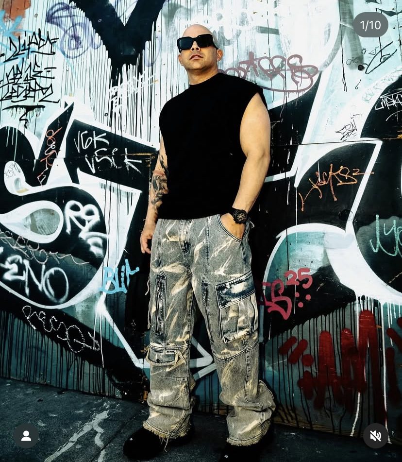 Look streetwear con camiseta negra sin mangas y cargo denim frente a un muro de graffiti
